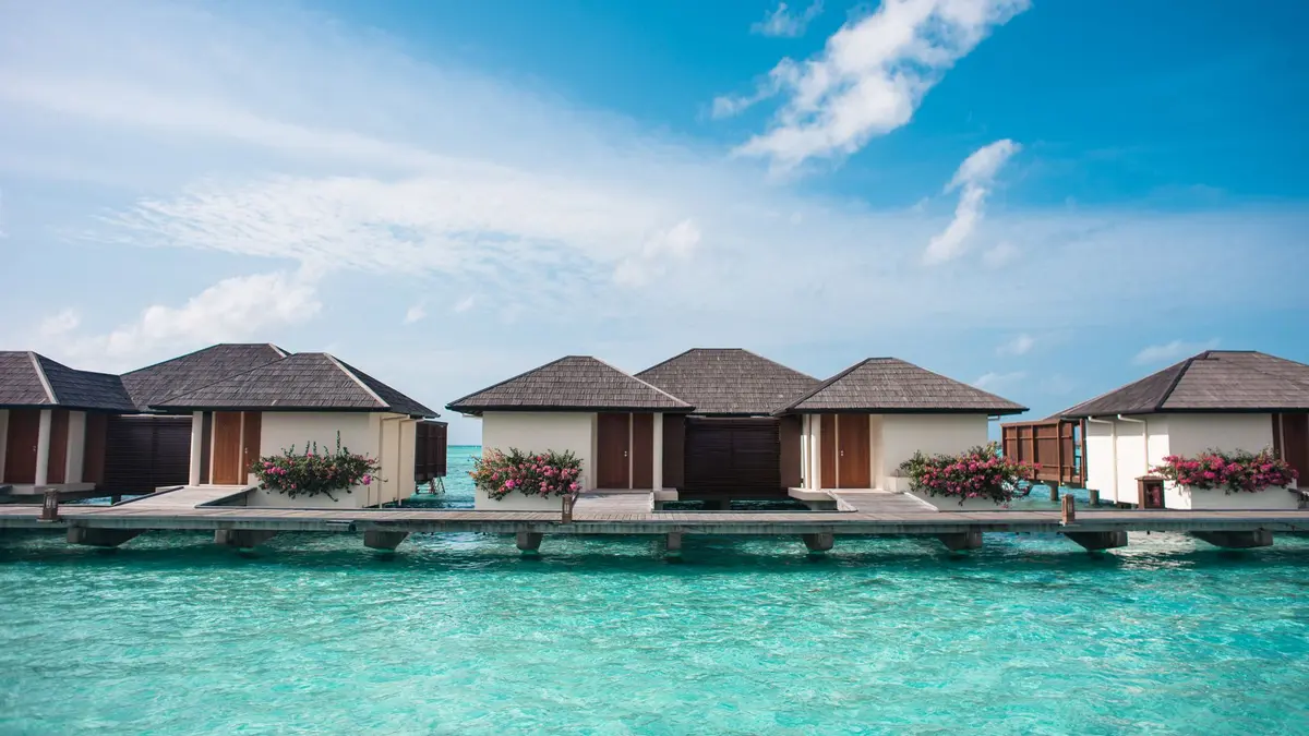 Turquoise lagoon and white sand beach in the Maldives with a traditional dhoni boat and overwater bungalows in the distance