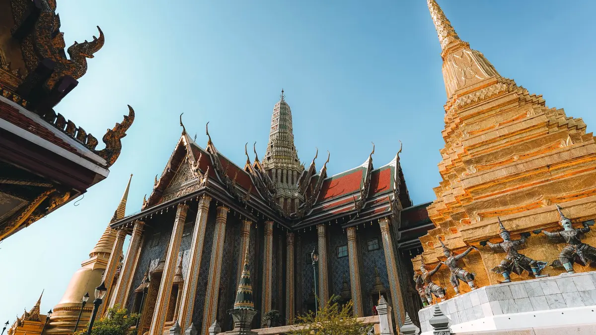 Golden spires of Bangkok's Grand Palace glowing against a twilight sky with the Chao Phraya River in the foreground
